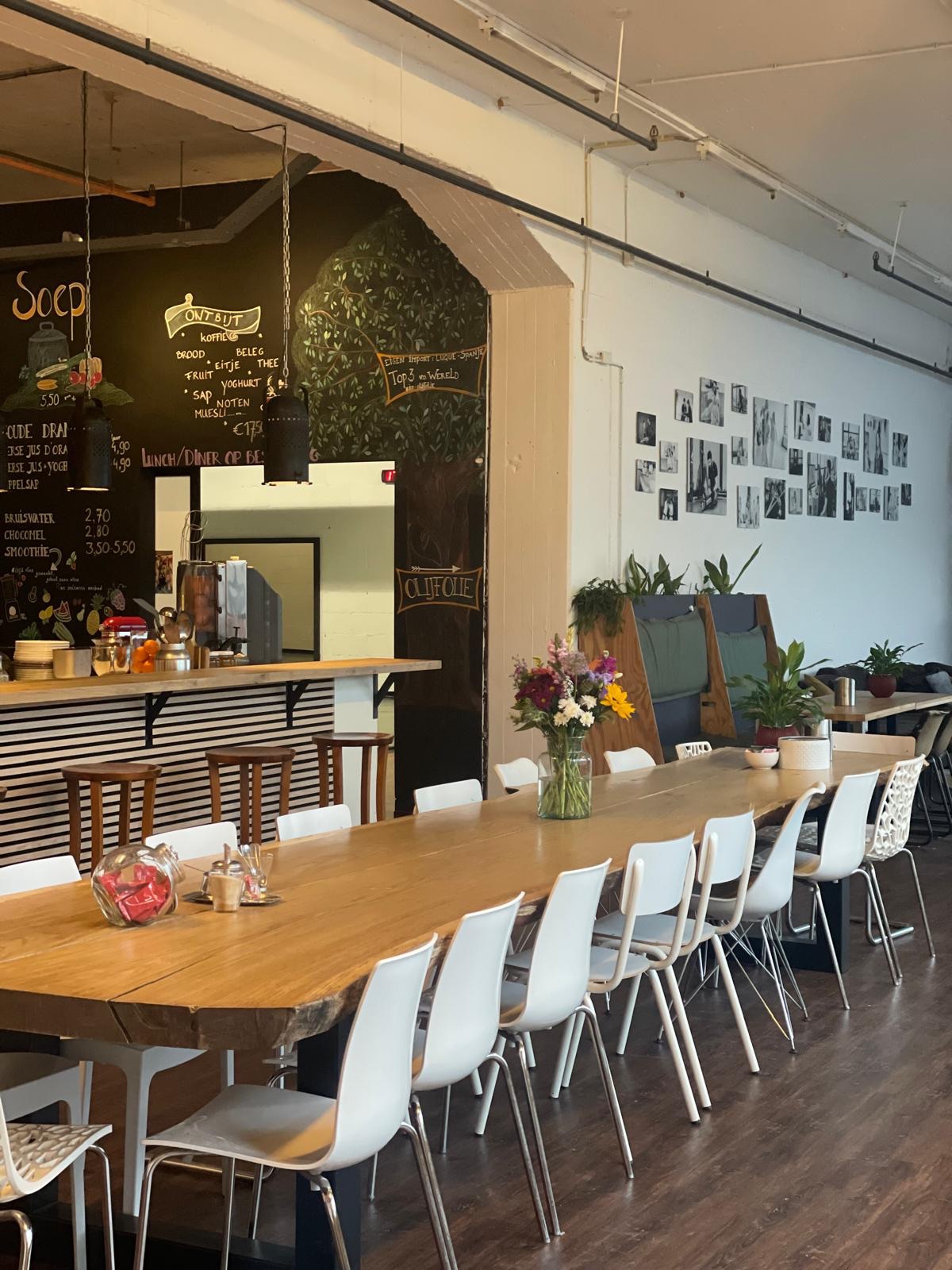 De lange tafel van B-Food in de oude textielfabriek van B-me in Tilburg, gedekt met bloemen, met het krijtbordmenu op de achtergrond